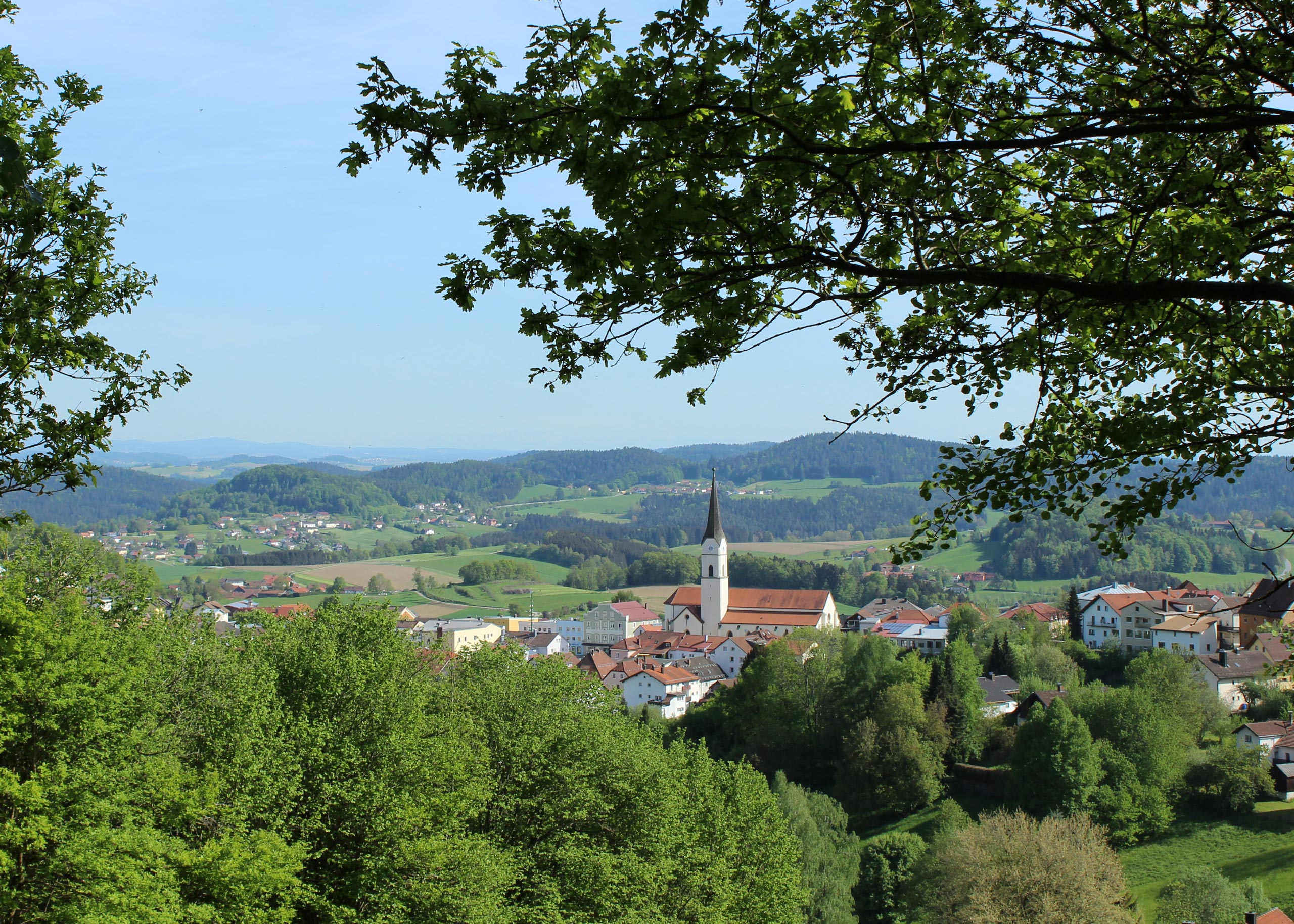 Blick auf ein Dorf mit einer Kirche und umliegenden grünen Landschaften in der Ferne.