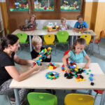 Kinder und Betreuerin spielen mit bunten Bauklötzen in einem Raum einer Kindertagesstätte.
