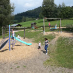 Spielplatz mit einer blauen Rutsche, Schaukeln und Kindern, die spielen.