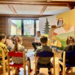 Eine Gruppe von Kindern sitzt in einem Raum und hört einem Geschichtenerzähler zu, der vor ihnen sitzt.