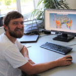 Mann mit Bart sitzt an einem Schreibtisch und arbeitet an einem Computer mit Konstruktionssoftware.