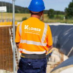 Bauarbeiter mit orangefarbener Sicherheitsweste und blauer Schutzhelm auf einer Baustelle.