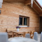 Holz-Cottage mit einem Tisch und Stühlen im Vordergrund, dekoriert mit einer Vase und Blumen.
