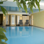 Innenansicht eines Wellnessbereichs mit einem blauen Pool und zwei Liegen.