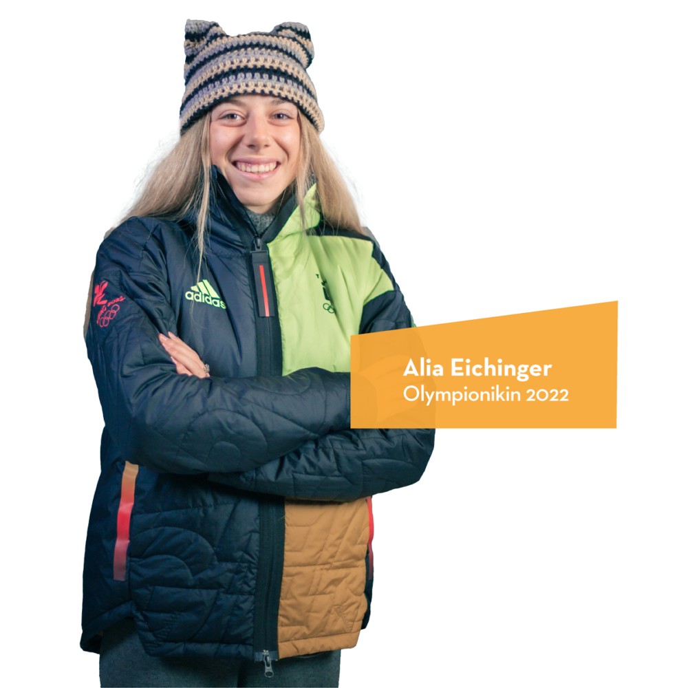 Alia Eichinger trägt eine farbige Olympiade-Jacke und eine Mütze mit Ohren.