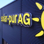 Leuchtendes Unternehmensschild mit dem Namen 'solar-pur AG' und einer Sonne auf der Fassade.