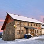 Das Dreisesselhaus, ein steinernes Gebäude mit einem schneebedeckten Dach und einer Holzveranda.