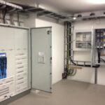 Ein Raum mit offenen Verteilerkästen und elektrischen Schaltanlagen an den Wänden.