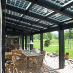 Überdachte Terrasse mit schwarzen Balken und Solarpanelen auf dem Dach.