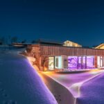 Moderne Architektur eines Hauses mit beleuchtetem Eingangsbereich in einer verschneiten Landschaft bei Nacht.