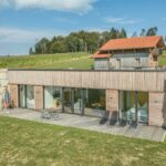 Moderne Holzarchitektur mit großen Fenstern und einer Terrasse, umgeben von Natur.