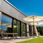 Moderne Holzfassade eines Hauses mit Sonnenschirmen und Gartenmöbeln auf einer Terrasse.