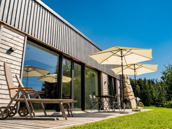 Moderne Holzfassade eines Hauses mit Sonnenschirmen und Gartenmöbeln auf einer Terrasse.