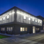 Ein modernes Gebäude mit beleuchteter Fassade und großen Fenstern bei Nacht.