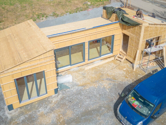 Drohnenaufnahme eines im Bau befindlichen regionalen Pavillons mit Holzverkleidung und großen Fenstern.