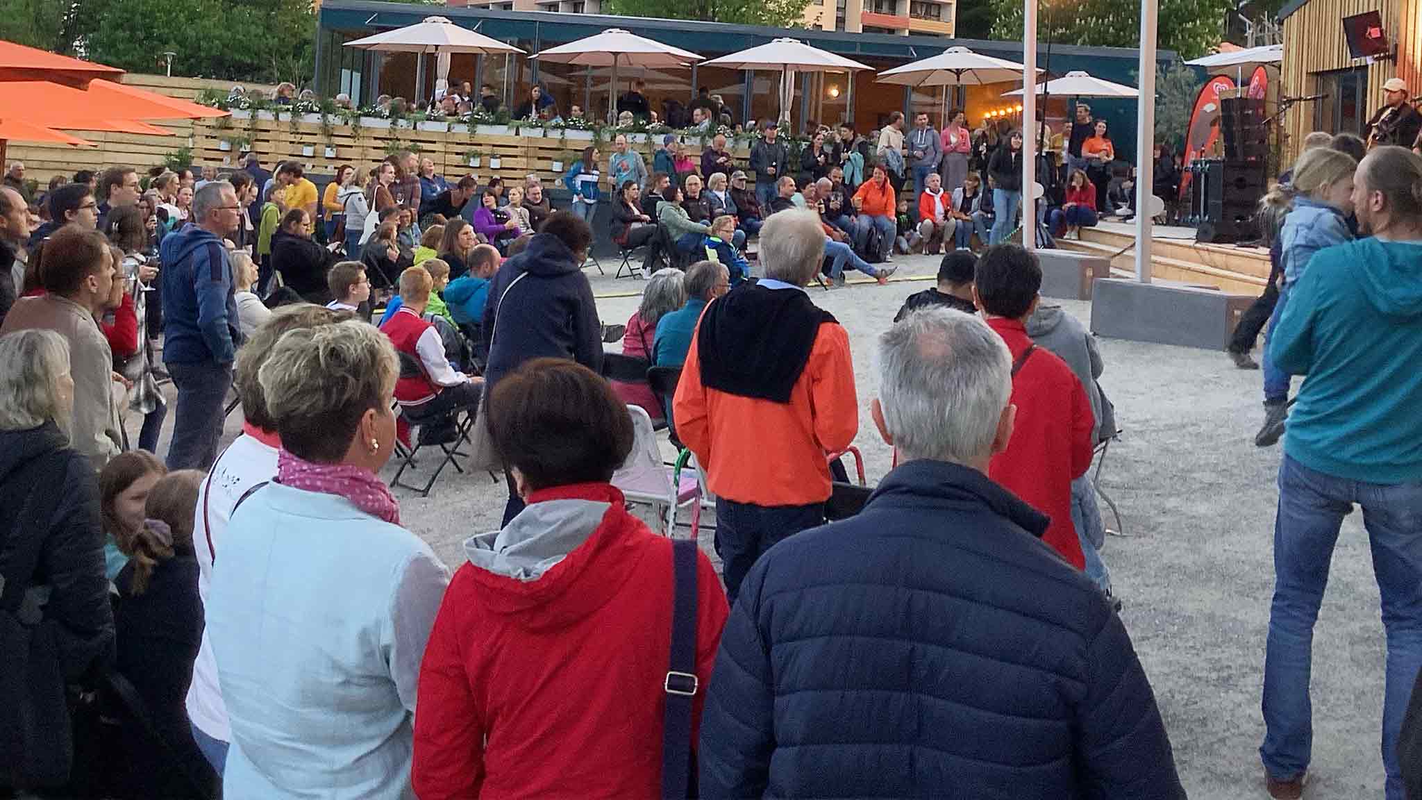Eine große Menschenmenge versammelt sich bei einer Veranstaltung im Freien mit Stühlen und einer Bühne.