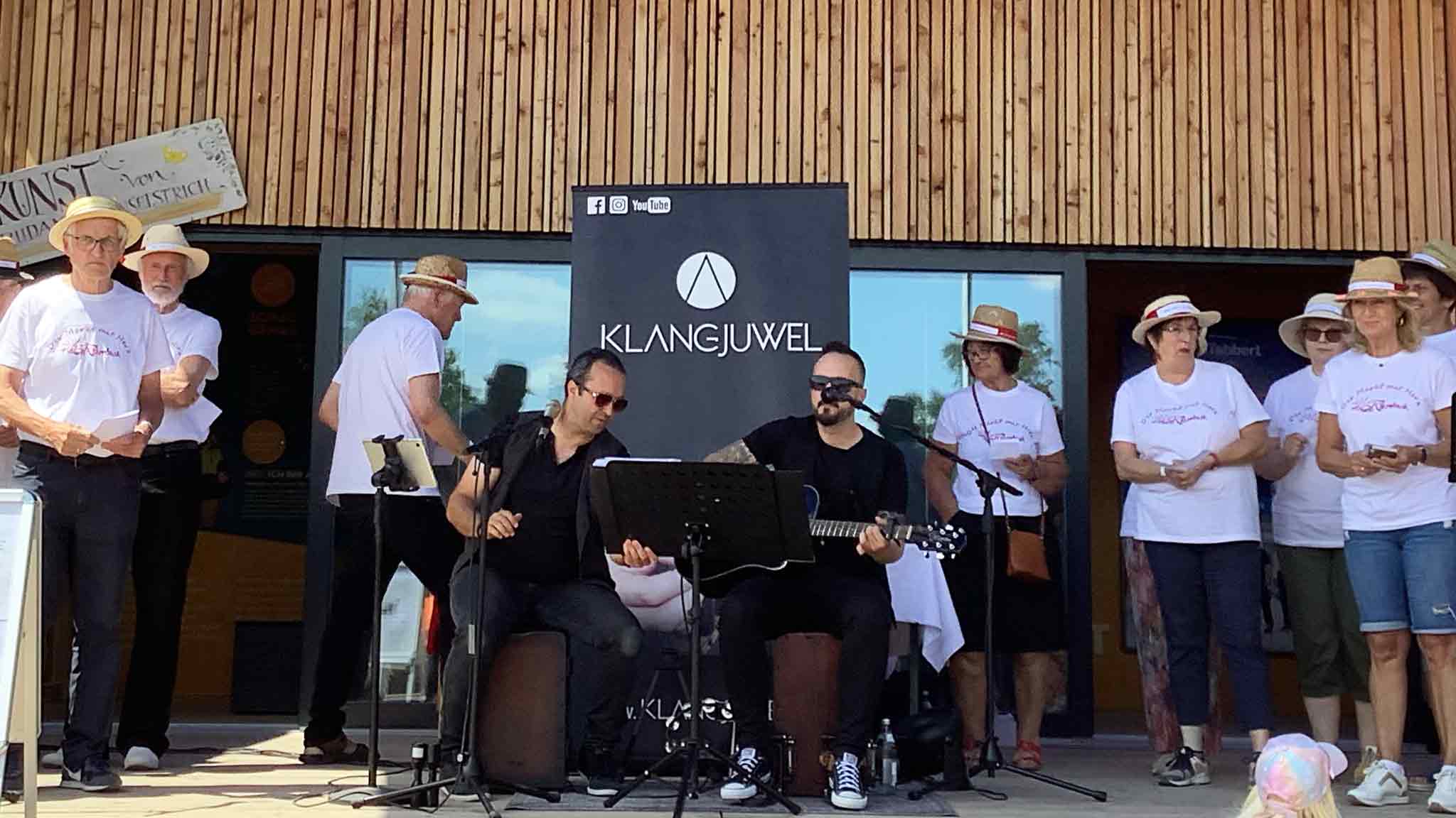 Zwei Musiker mit Gitarre und Gesang bei einer Live-Aufführung vor einer Gruppe von Menschen.