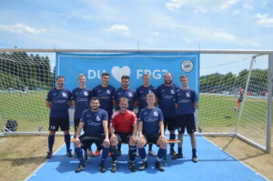 Eine Fußballmannschaft posiert vor einem Tor auf dem Spielfeld, alle in blauen Trikots.
