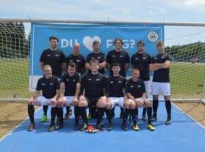 Eine Fußballmannschaft in schwarzen Trikots steht vor einem Tor auf dem Spielfeld.