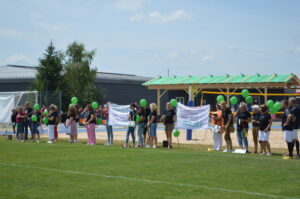 Eine Gruppe von Menschen mit grünen Ballons steht auf einem Sportfeld und hält Banner.