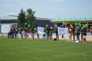 Gruppe von Menschen mit grünen Ballons und Bannern auf einem Sportplatz im Freien.