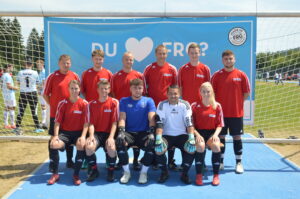 Eine Fußballmannschaft in roten Trikots steht vor einem Tor auf einem Sportplatz.