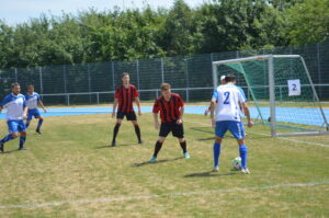 Zwei Fußballspieler in roten und blauen Trikots stehen sich auf dem Spielfeld gegenüber.