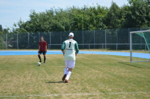 Zwei Fußballspieler auf einem Spielfeld, einer mit der Nummer 1 im Tor und der andere in einem roten Trikot.