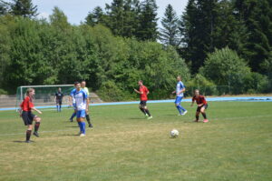 Fußballspiel mit Spielern in blauen und roten Trikots auf einem Rasenplatz.