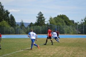 Zwei Fußballspieler in blauen Trikots und ein Spieler in rotem Trikot auf dem Spielfeld.