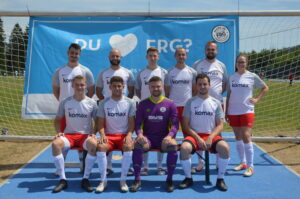 Eine Fußballmannschaft in weißen Trikots mit roten Shorts steht vor einem Tor.