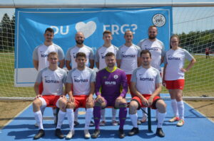 Eine Fußballmannschaft in weißen Trikots mit roten Hosen und komax-Logo auf dem Platz.