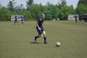 Ein Fußballspieler in blauer Sportkleidung läuft mit einem Ball auf einem Kunstrasenplatz.