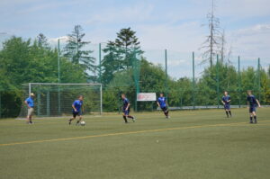 Spieler in blauen Trikots, die auf einem Fußballplatz spielen, mit einem Tor im Hintergrund.