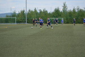 Spieler in blauen Trikots, die während eines Fußballtrainings auf einem Kunstrasenplatz laufen und einen Ball verfolgen.
