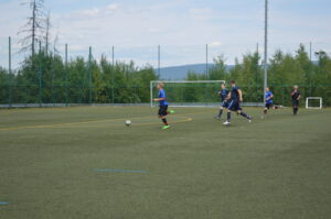 Spieler in blauen Trikots laufen auf einem Fußballfeld mit einem Ball.