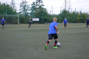 Spieler in blauen Trikots und schwarze Hosen auf einem Kunstrasenplatz während eines Fußballspiels.