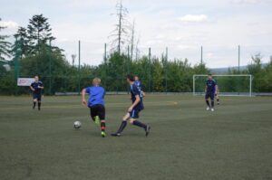 Zwei Spieler in blauen Trikots, die einen Fußball auf einem Kunstrasenplatz spielen.