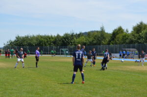 Spieler in blauen Trikots während eines Fußballspiels auf einem Sportplatz.