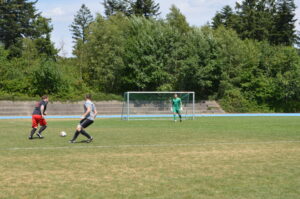 Zwei Spieler beim Fußballspiel auf einem Sportplatz mit einem Tor im Hintergrund.