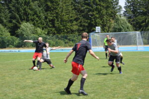 Zwei Gruppen von Spielern, die ein Fußballspiel auf einem Rasenplatz spielen, mit einem Tor im Hintergrund.