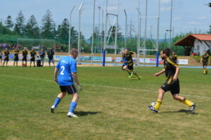 Zwei Fußballspieler im Wettkampf auf einem Sportplatz, einer in blauer und der andere in schwarzer und gelber Uniform.