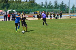 Zwei Fußballspieler, einer in blauem Trikot und der andere in schwarzem Trikot, kämpfen um den Ball auf einem Spielfeld.
