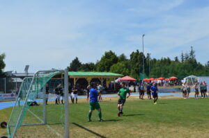 Torwart in blauer Ausrüstung fängt den Ball während eines Fußballspiels auf einem Sportplatz.