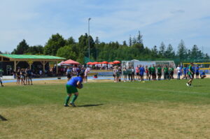 Ein Fußballspieler in blauer und grüner Ausrüstung bereitet sich auf einen Wurf auf einem Sportplatz vor.