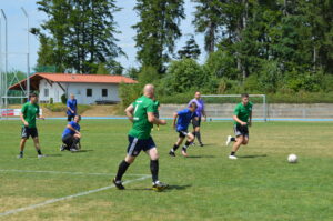 Eine Gruppe von Spielern in grünen und blauen Trikots spielt Fußball auf einem Rasenplatz.