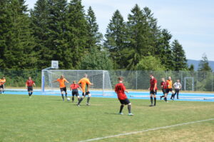 Fußballspieler in orange und schwarz auf einem Spielfeld mit Tor im Hintergrund.