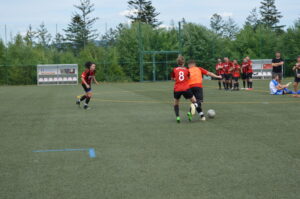 Zwei Spielerinnen im Fußballspiel auf einem Kunstrasenplatz, eine in orange und die andere in rot mit der Nummer 8.