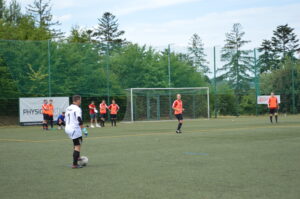 Spieler in weißen und orangefarbenen Trikots auf einem Kunstrasenplatz während eines Fußballspiels.