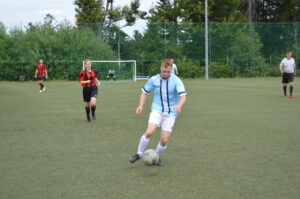 Ein Fußballspieler in hellblauem Trikot dribbelt den Ball auf einem Kunstrasenplatz.